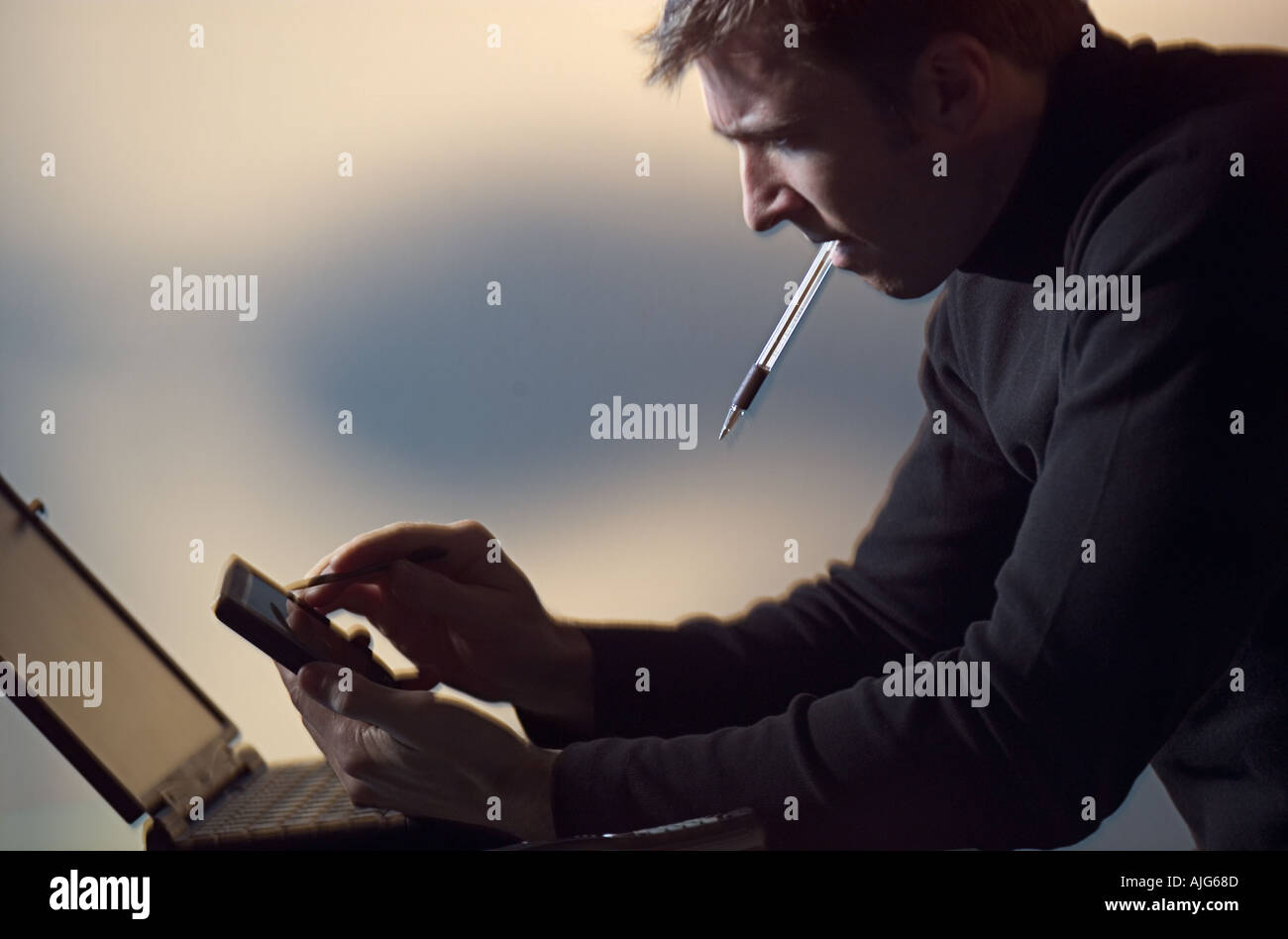 Man using PDA working on laptop computer in home office Stock Photo