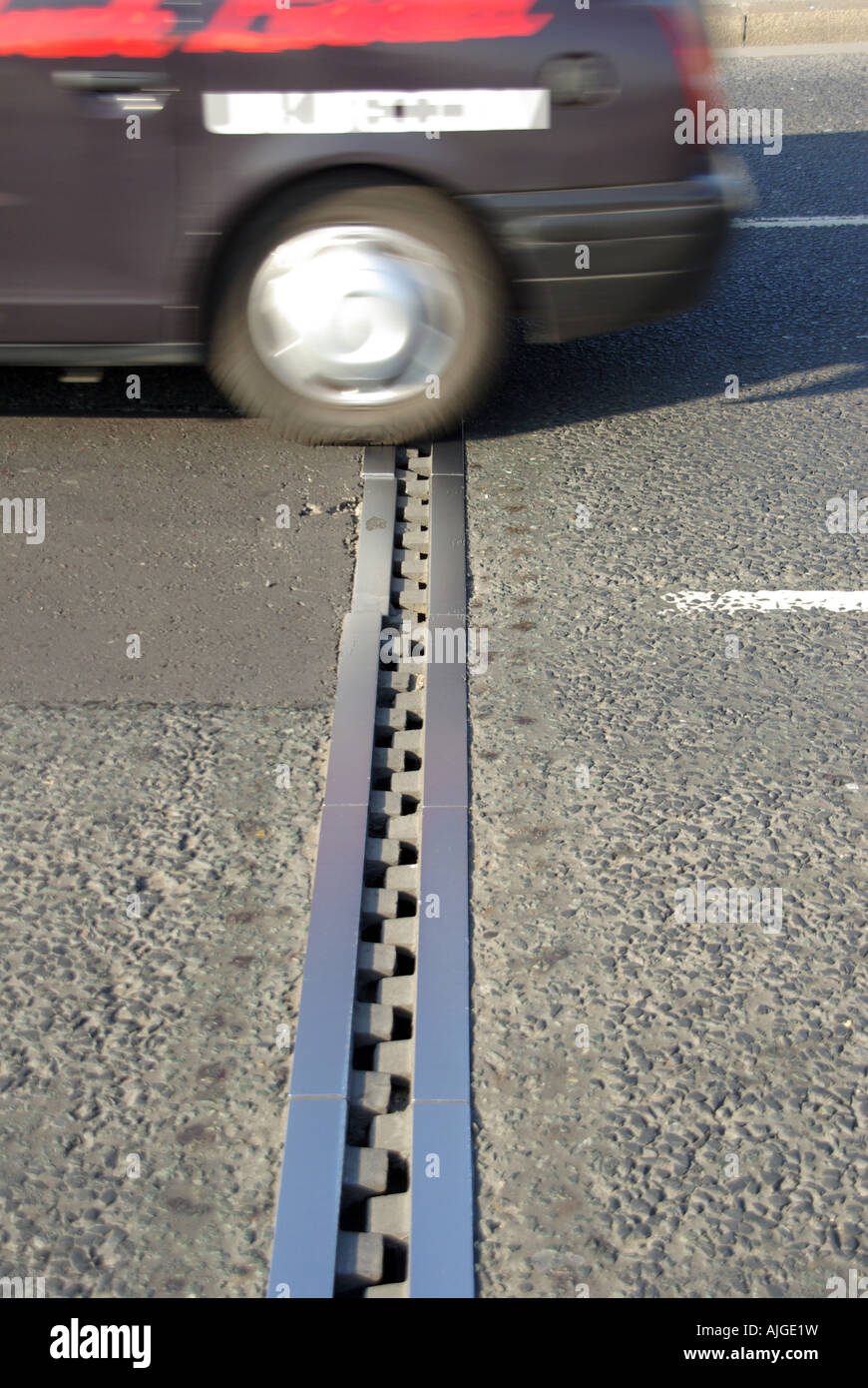 Close up of expansion joint & road surface tarmac with car wheel traffic passing over designed