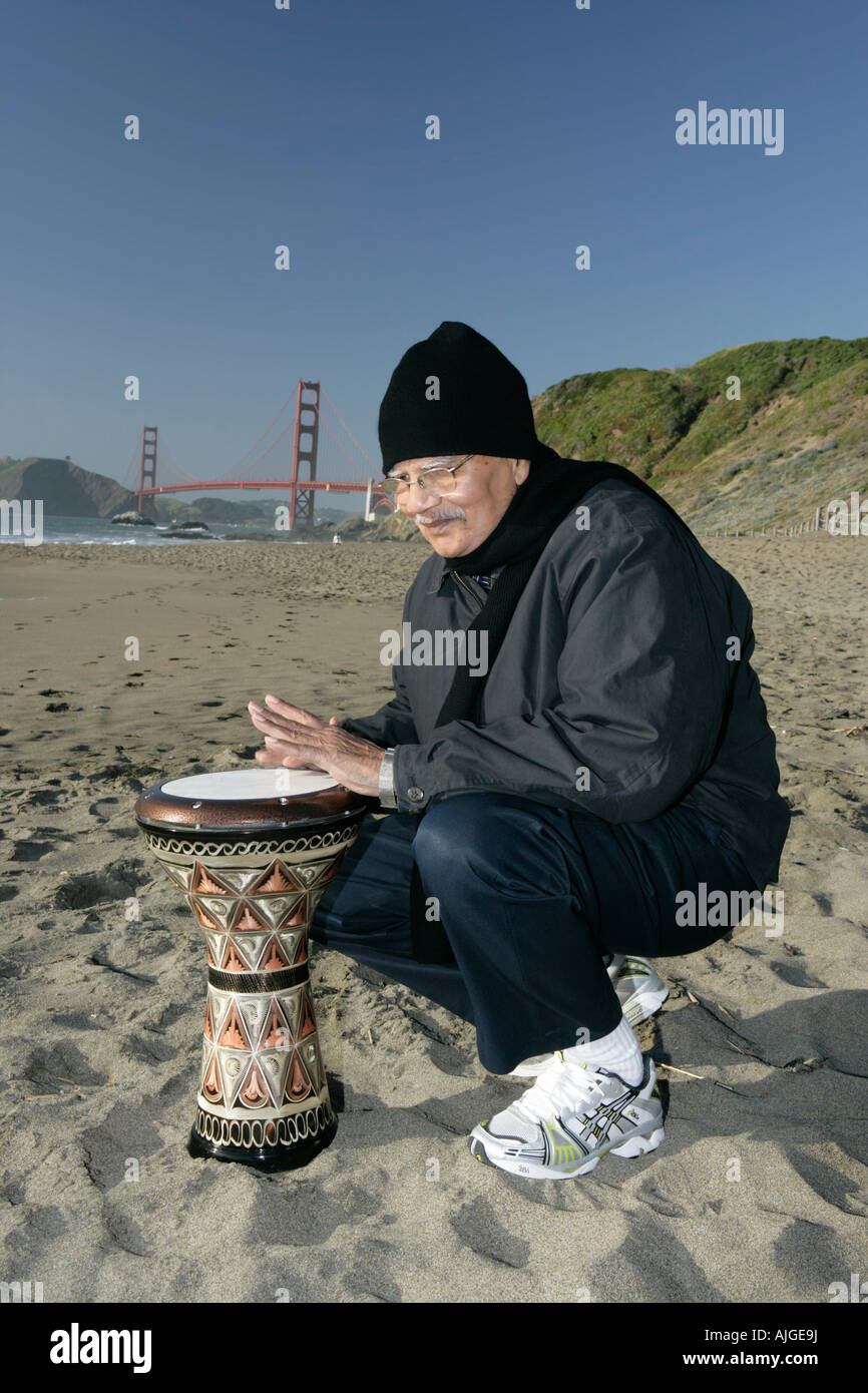 Elderly Indian happily playing turkish drums on baker beach in San Francisco California Stock Photo