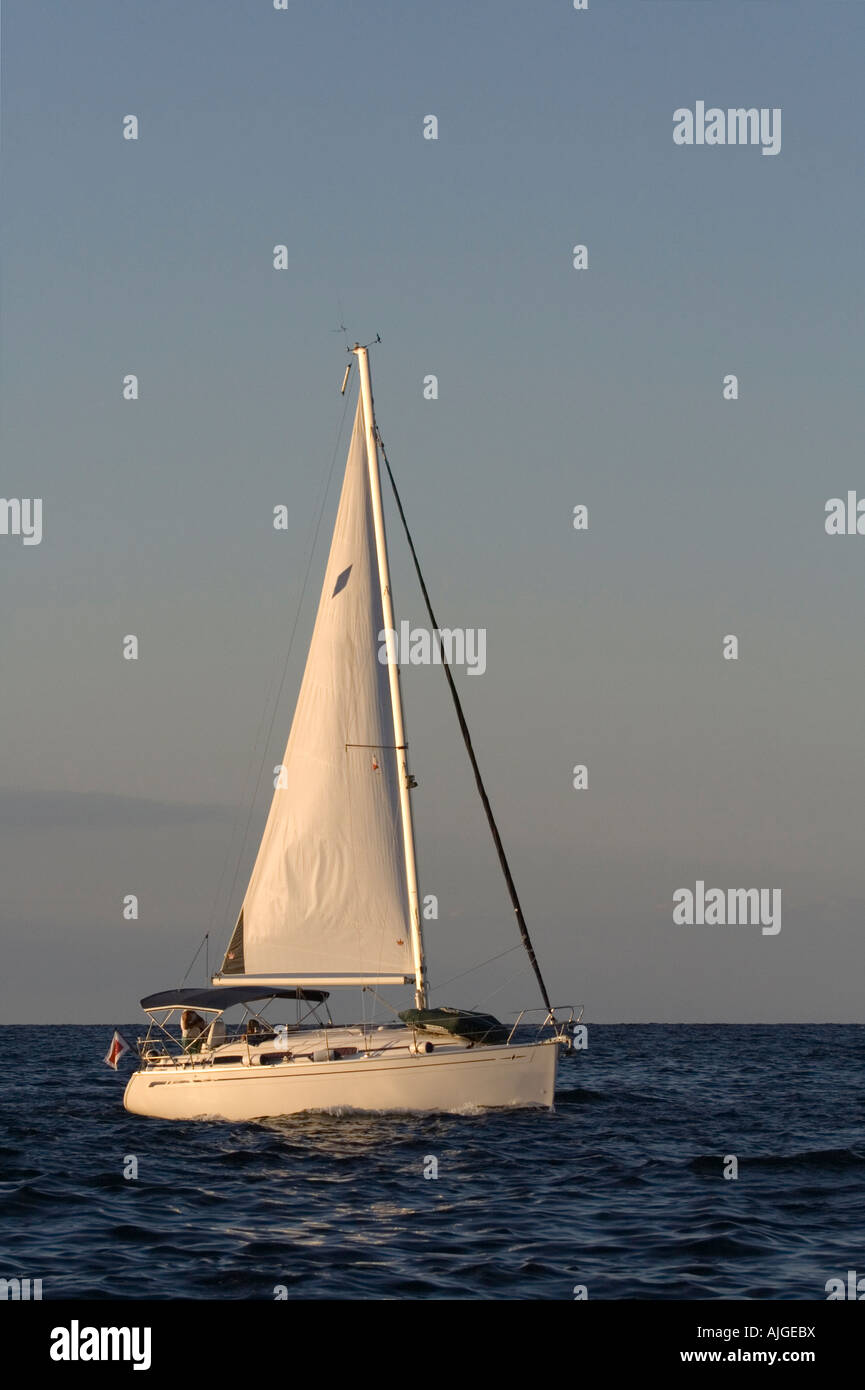 Yacht sailing at sunset. Proprietary markings removed and no faces visible. Stock Photo