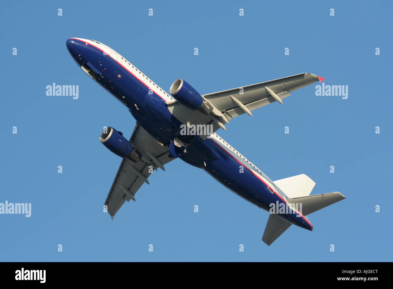 Air travel and commercial aviation. Airbus A320 passenger jet plane climbing in flight against a blue sky. No proprietary markings. Underside view. Stock Photo