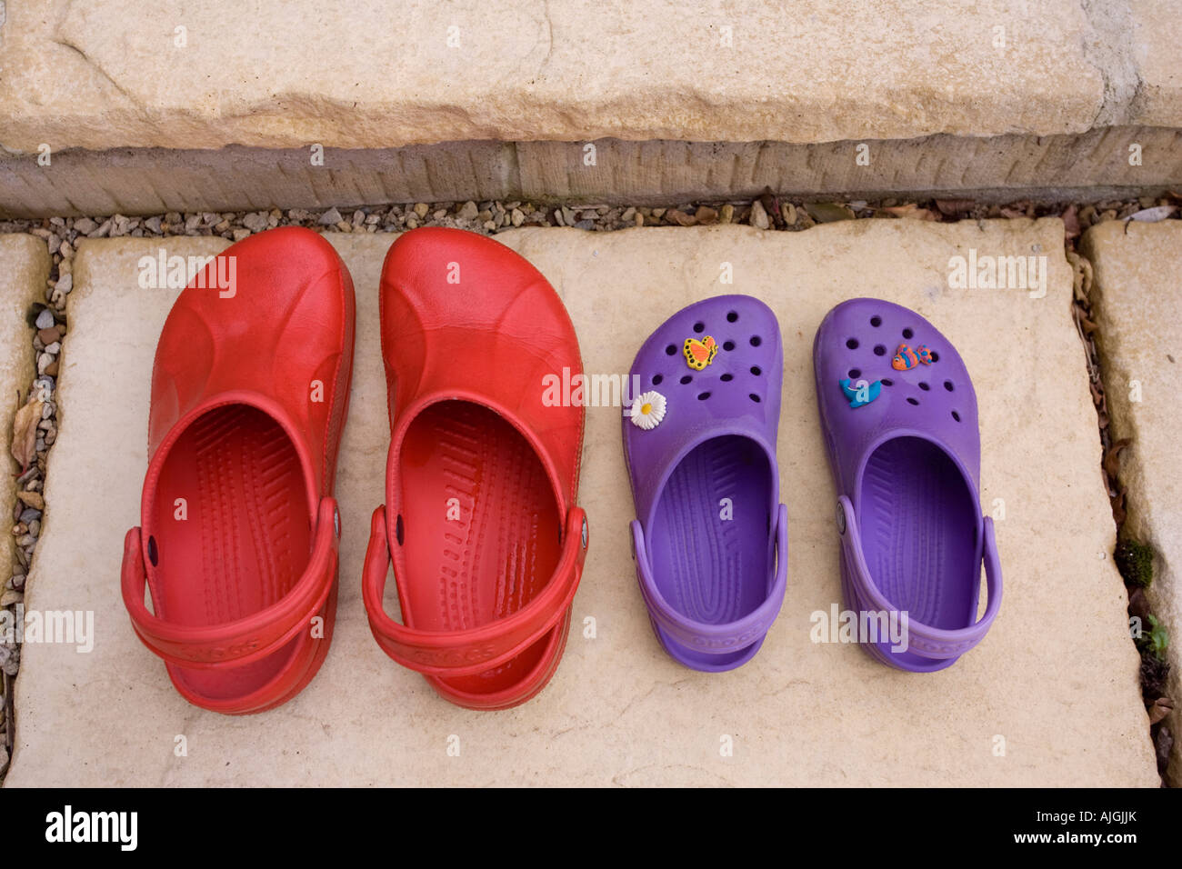 Pair of red adult croc sandals and purple child sandals on step outside door UK Stock Photo