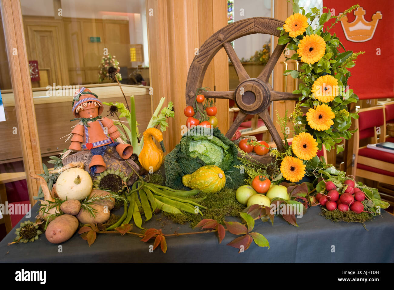 Attractive harvest festival display flower pot man fruit flowers and vegetables arranged around wagon wheel at church entrance Stock Photo