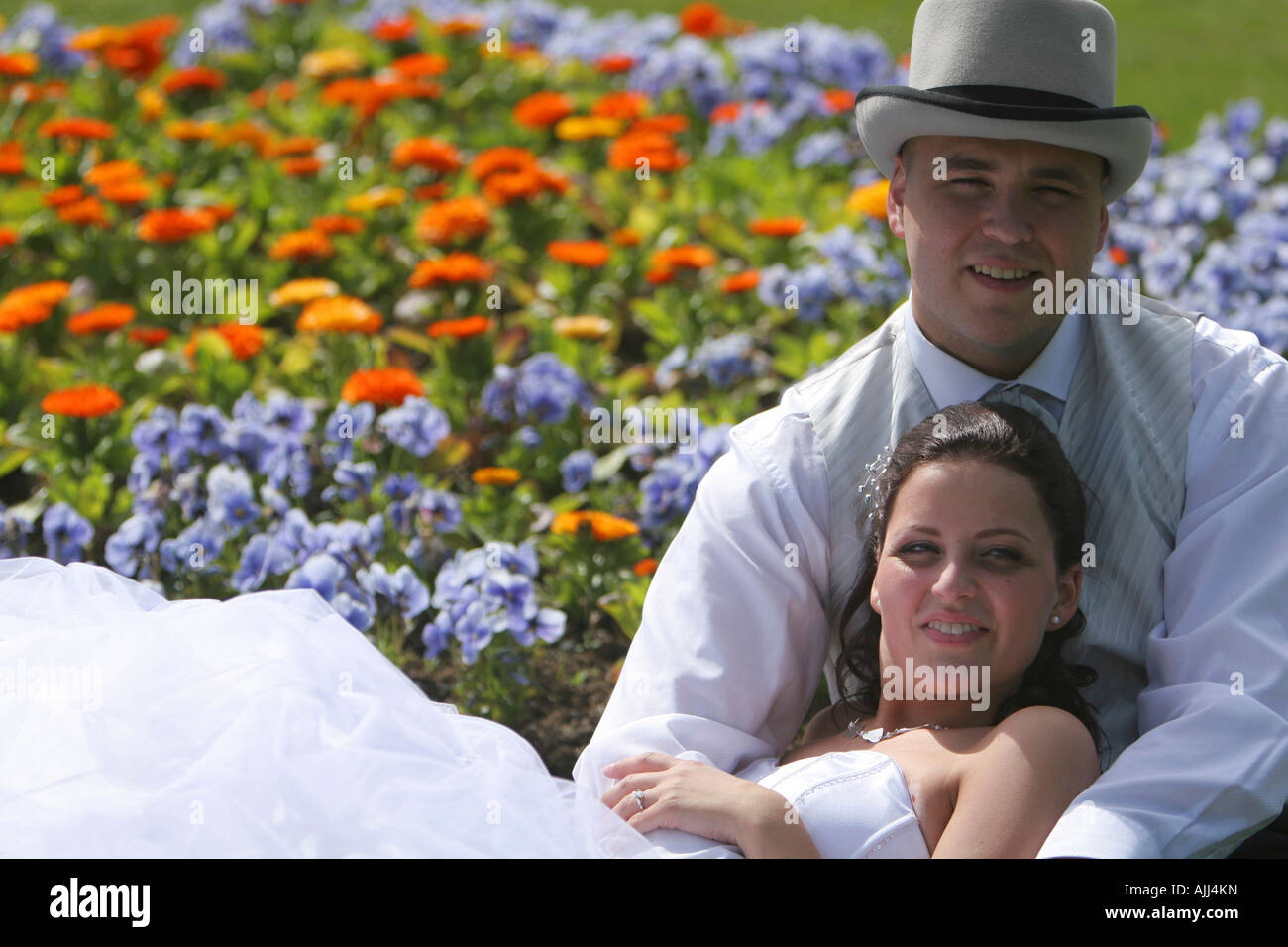 Newlywed young couple sitting amongst flowers just after the ceremony enjoying nice weather and looking towards the future Stock Photo