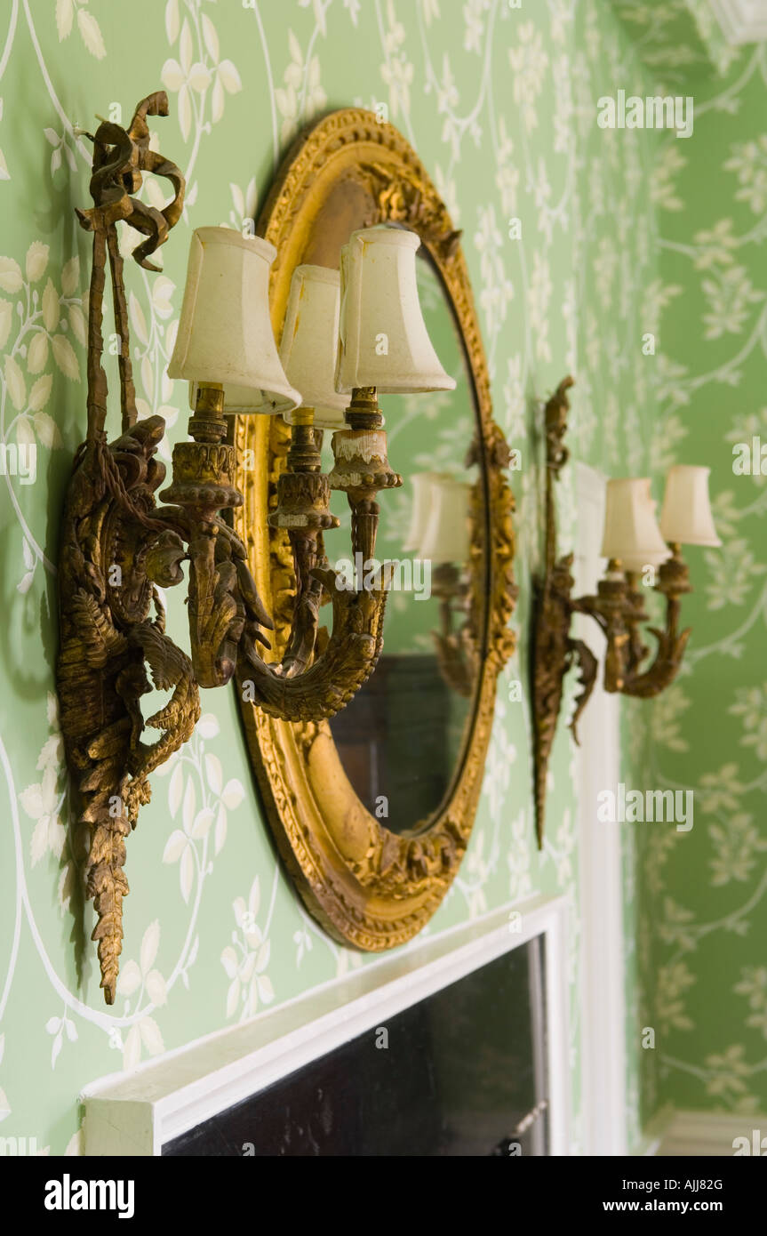 Gild mirror with sconce on either side on wall with green floral wallpaper in 17th century Irish castle Stock Photo