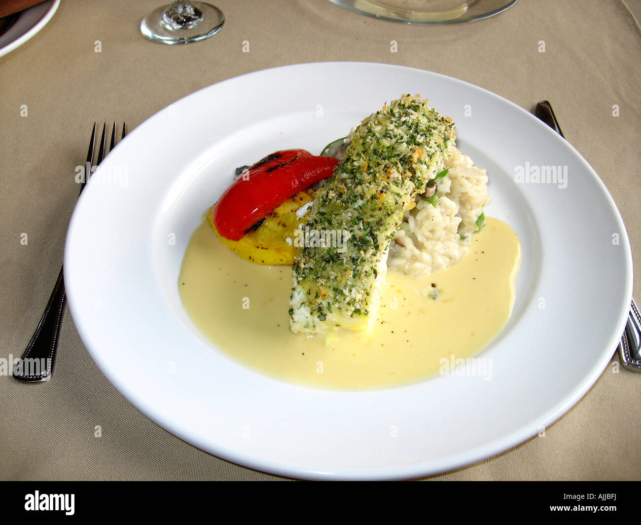 Cooked baked fish crusted halibut over risotto on a white ceramic plate Stock Photo