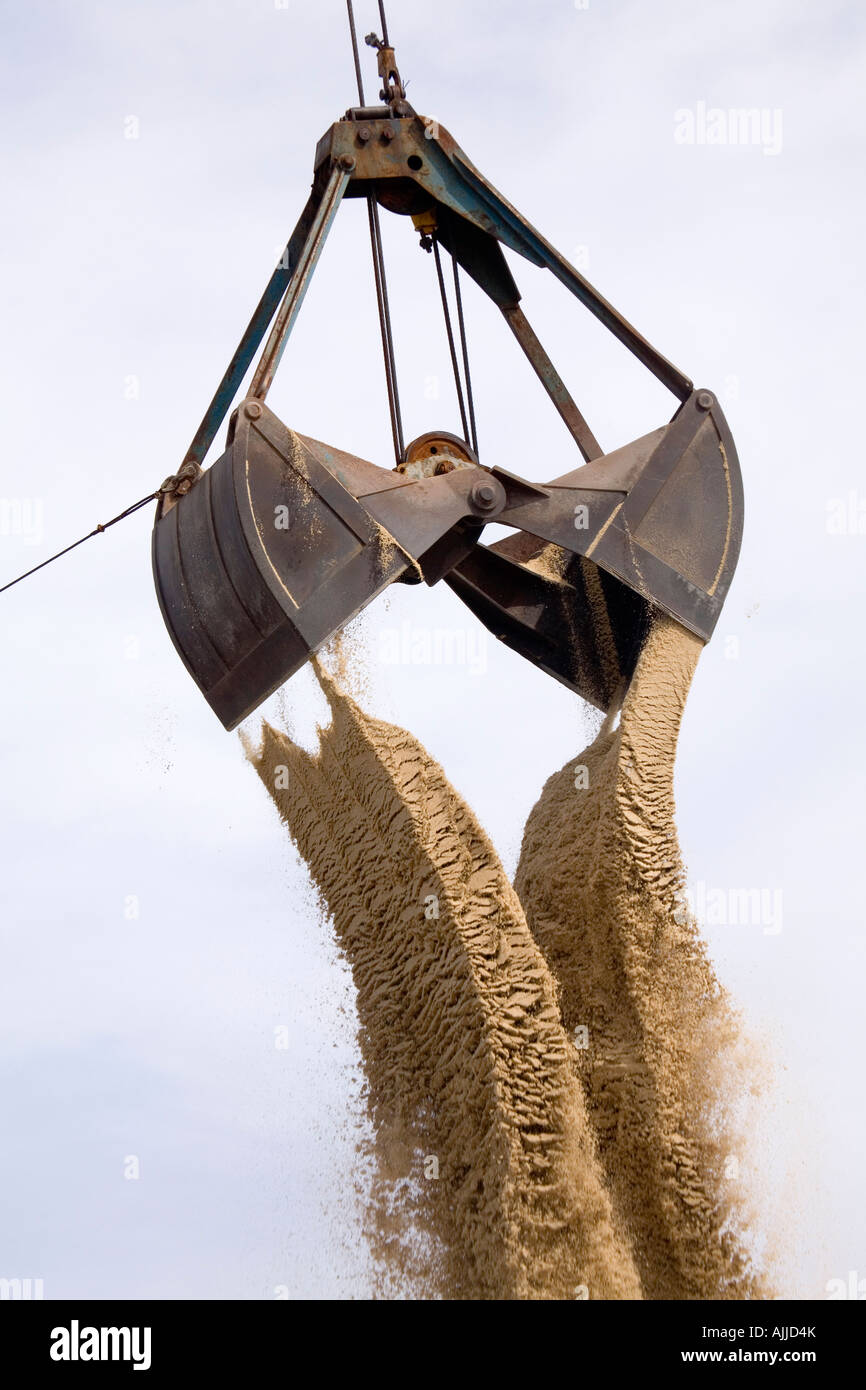 A clamshell bucketloader is seen dumping sand against a blue sky with light clouds. Stock Photo