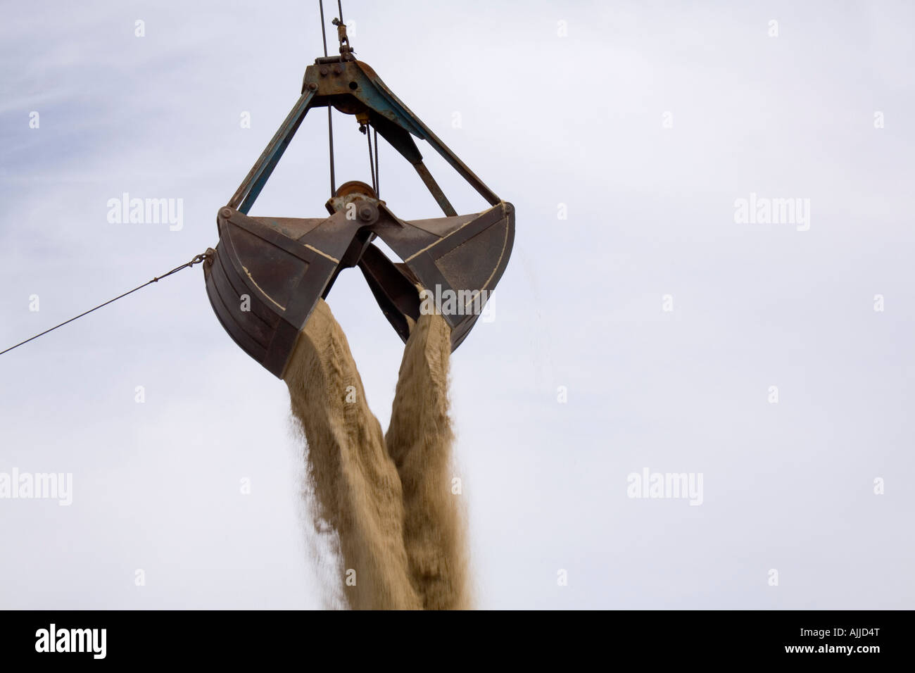 A clamshell bucket loader is seen dumping a load of sand after scooping it out of the hold of a cargo ship. Stock Photo
