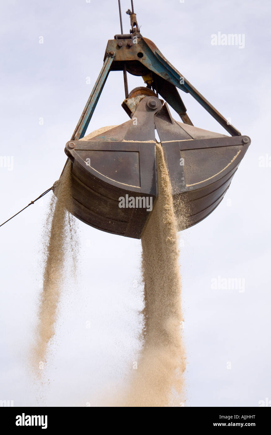 A clamshell bucketloader is seen about to dump a load of sand against a blue sky with light clouds. Stock Photo