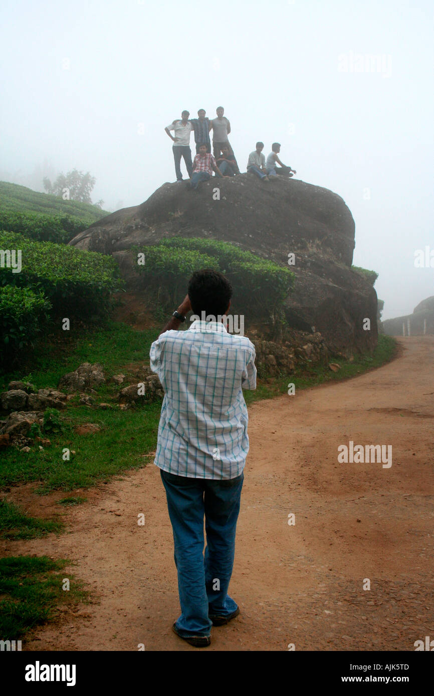 A young man taking a photograph of his friends posing over a rock, Munnar, Kerala, India Stock Photo