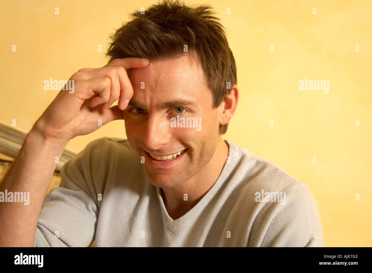 close up of a man looking at the camera smiling with a hand on his forehead Stock Photo