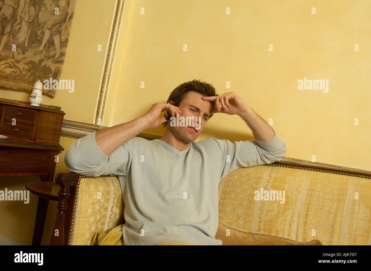 man sitting on a sofa while talking on the telephone looking thoughtful Stock Photo