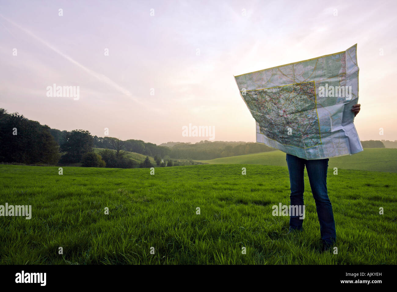 lost person standing on green meadow holding a large roadmap at sunset time Stock Photo