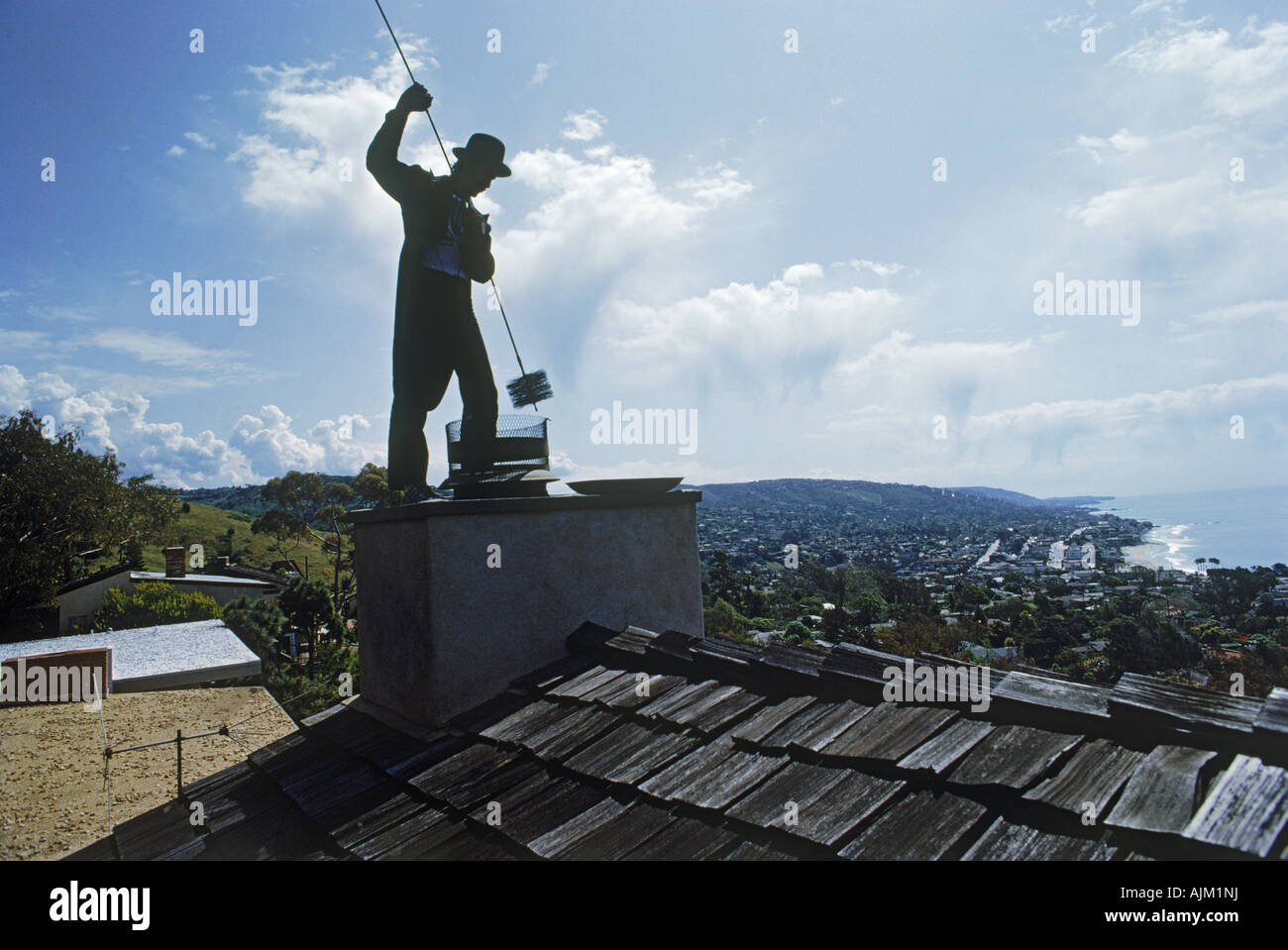 Chimney sweep at work on roof of California coastal home Stock Photo