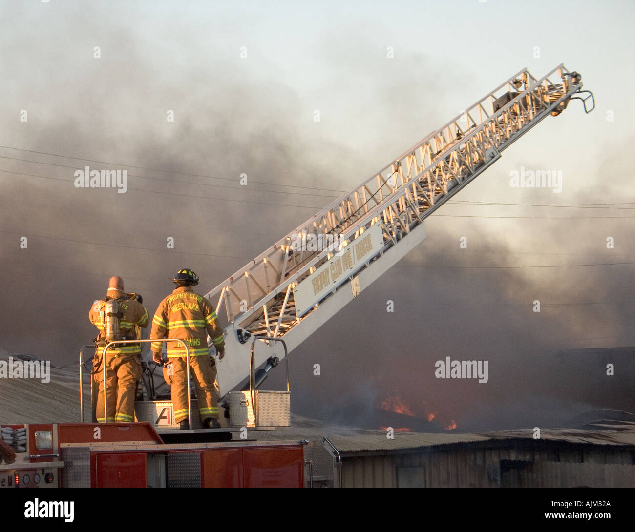 Two fire fighters working a ladder truck during an industrial fire ...