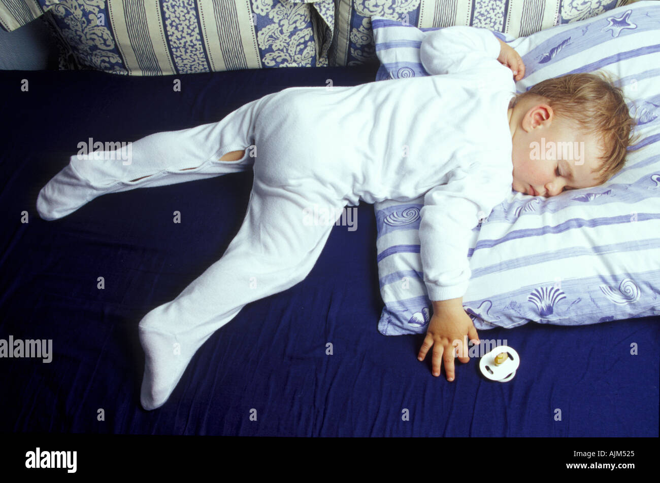 Sleeping baby boy on bed with pillow and white dress Stock Photo