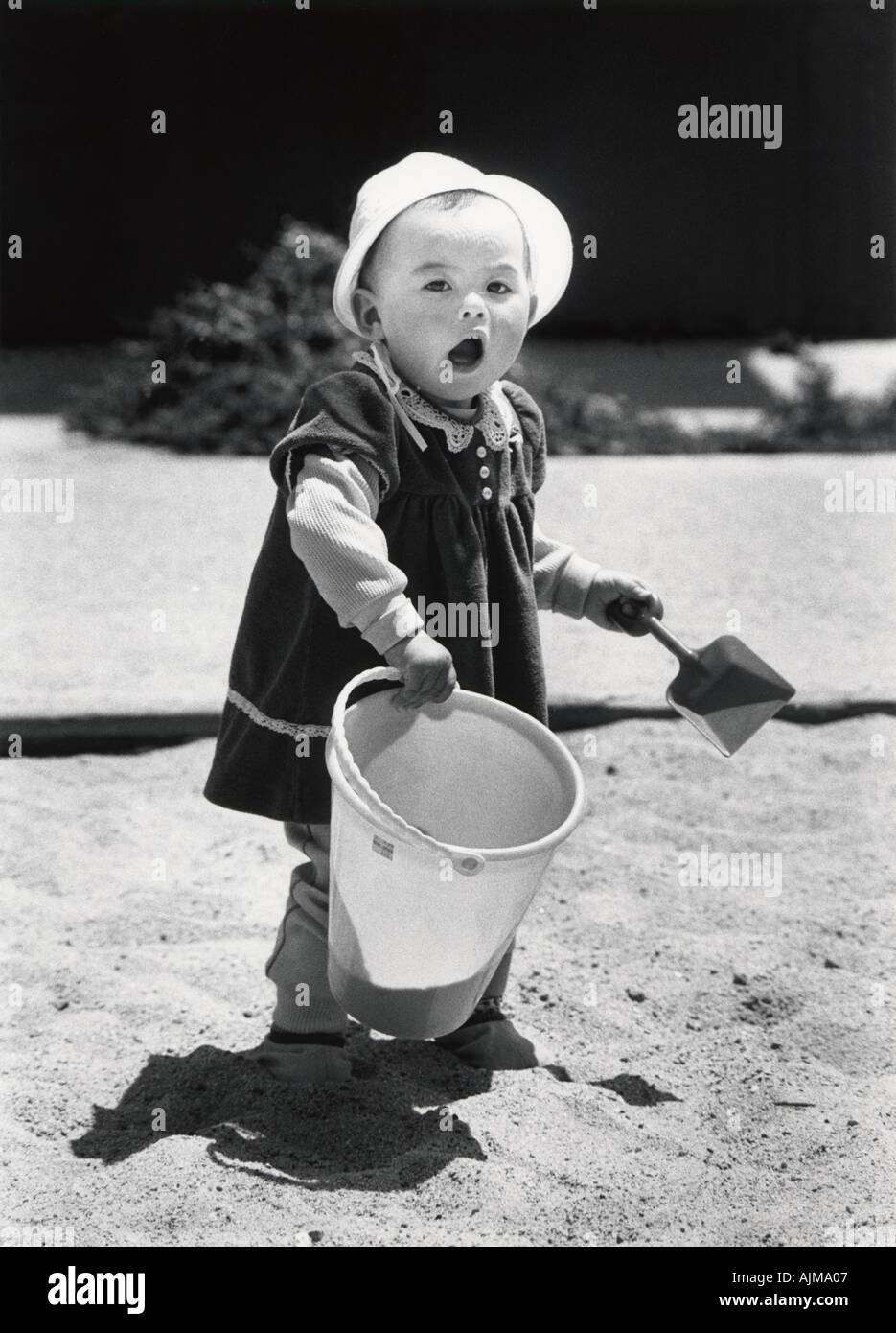 fourteen months old girl plays in a sandbox with plastic shovel and bucket in a park San Francisco California USA Stock Photo