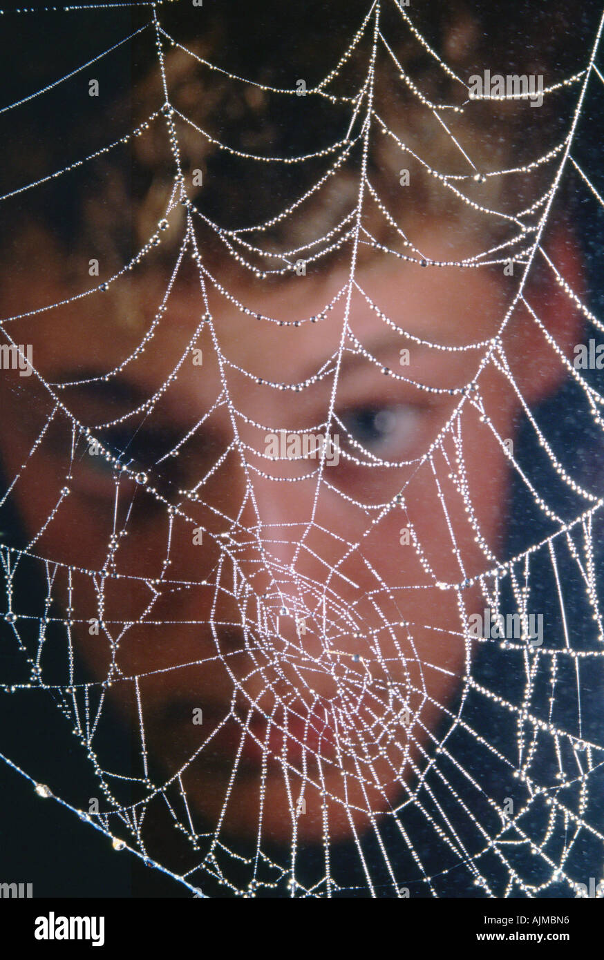 Close up of spiderweb with boy face observing it in the background Stock Photo