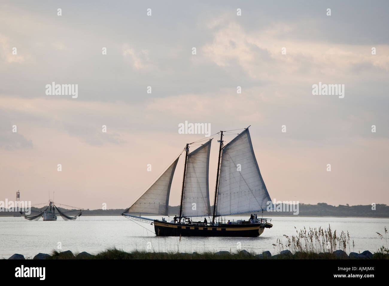 American schooner sailing ship with tourists returning to its harbor at sunset. Fishing vessel in the background. Stock Photo