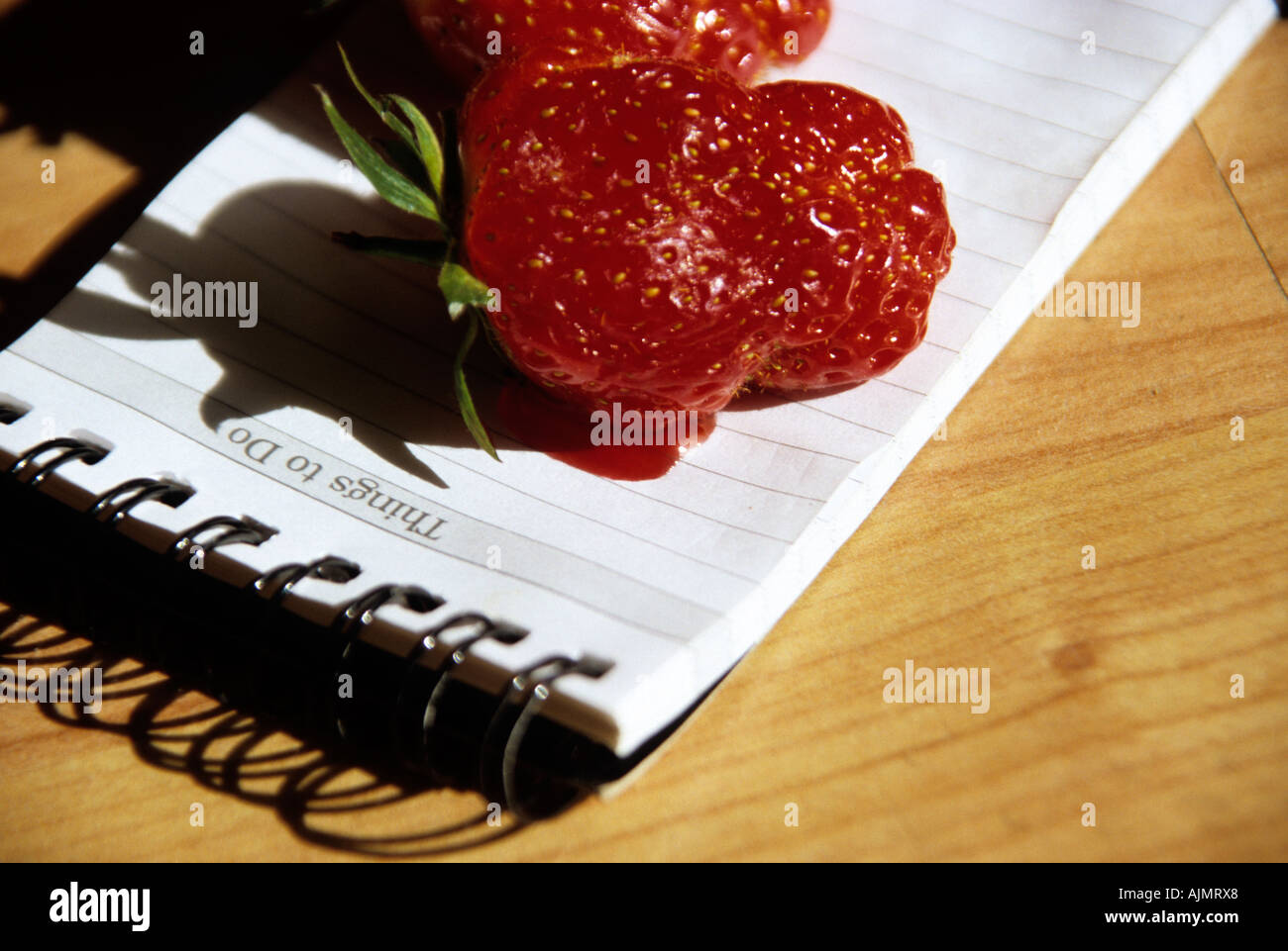 two strawberries freshly picked and resting on a notepad in the sunshine Stock Photo