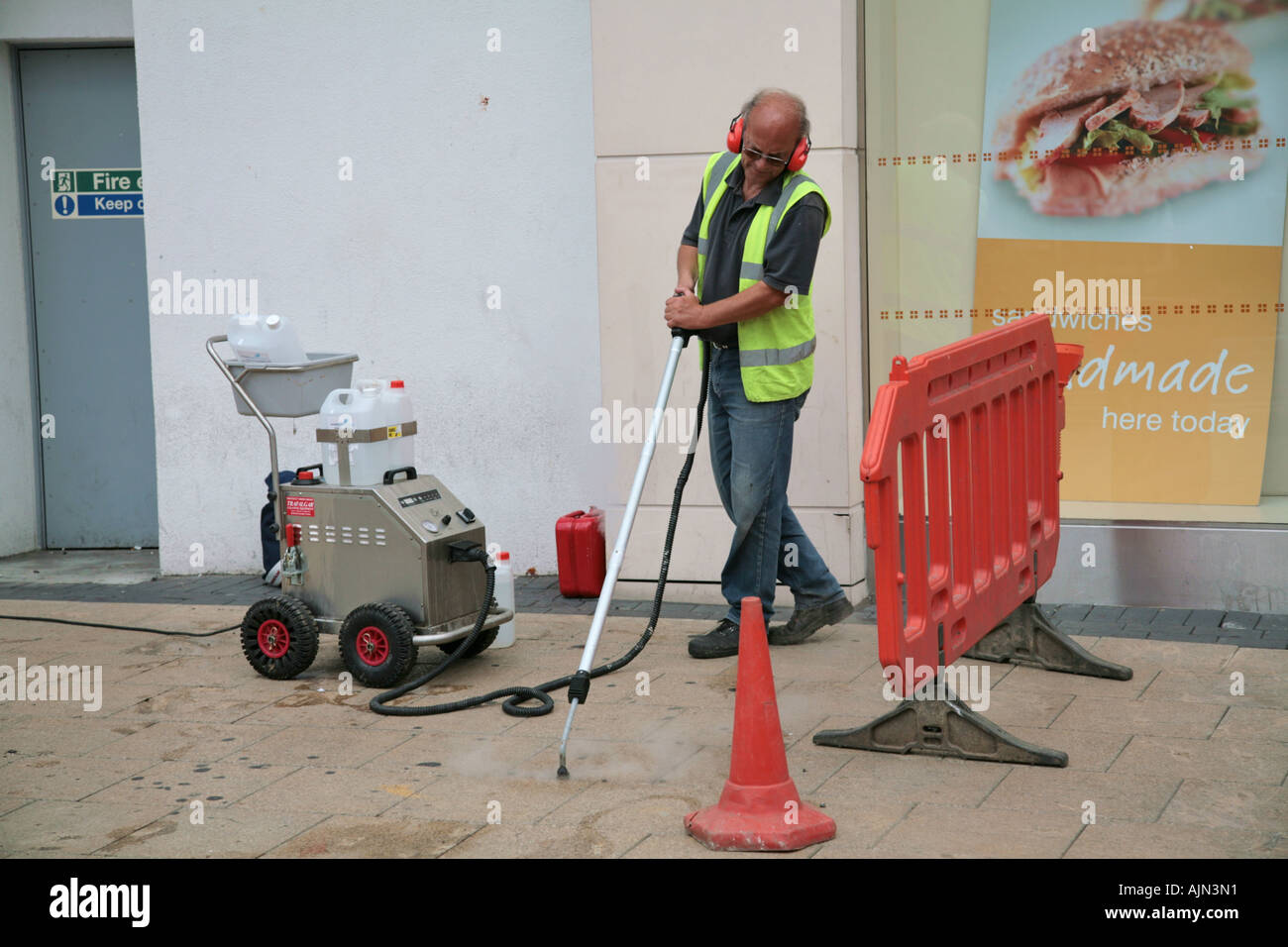 council worker steam-cleaning pavement in shopping centre Stock Photo