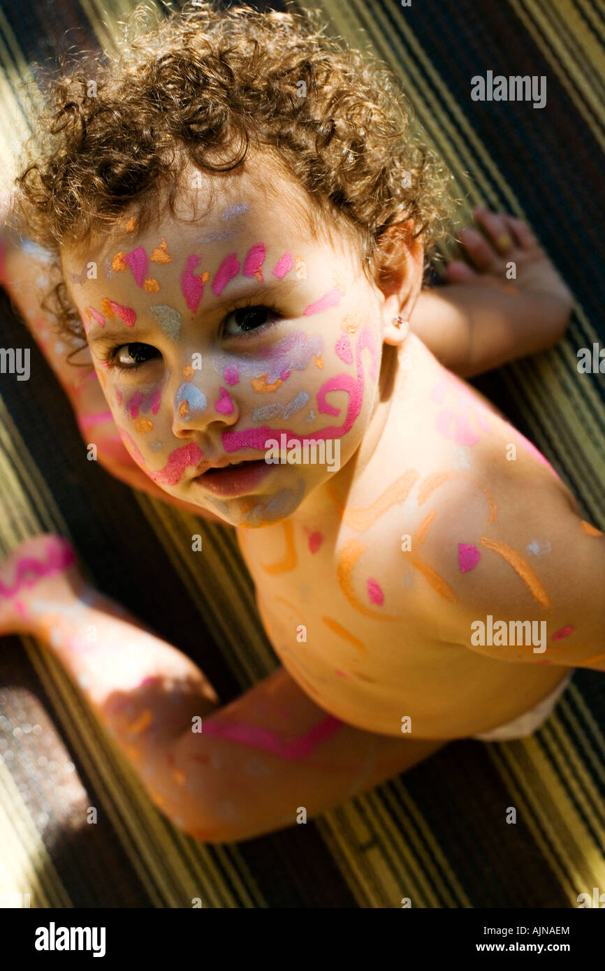 pondering beautiful girl with paint on her face and sunlight in her hair. covered in doodles she poses quietly for the camera Stock Photo