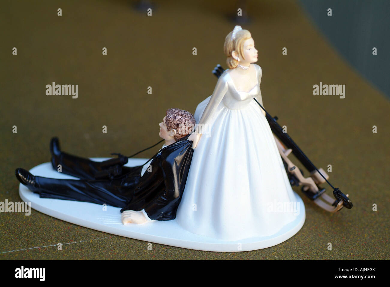 A Small plastic Cake topper with bride dragging groom. Bride has a Hunting  bow. Wedding humour Stock Photo - Alamy
