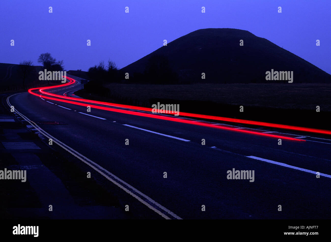 Traffic trails at dusk curving around Silbury Hill on the outskirts of Avebury in Wiltshire county England UK Stock Photo