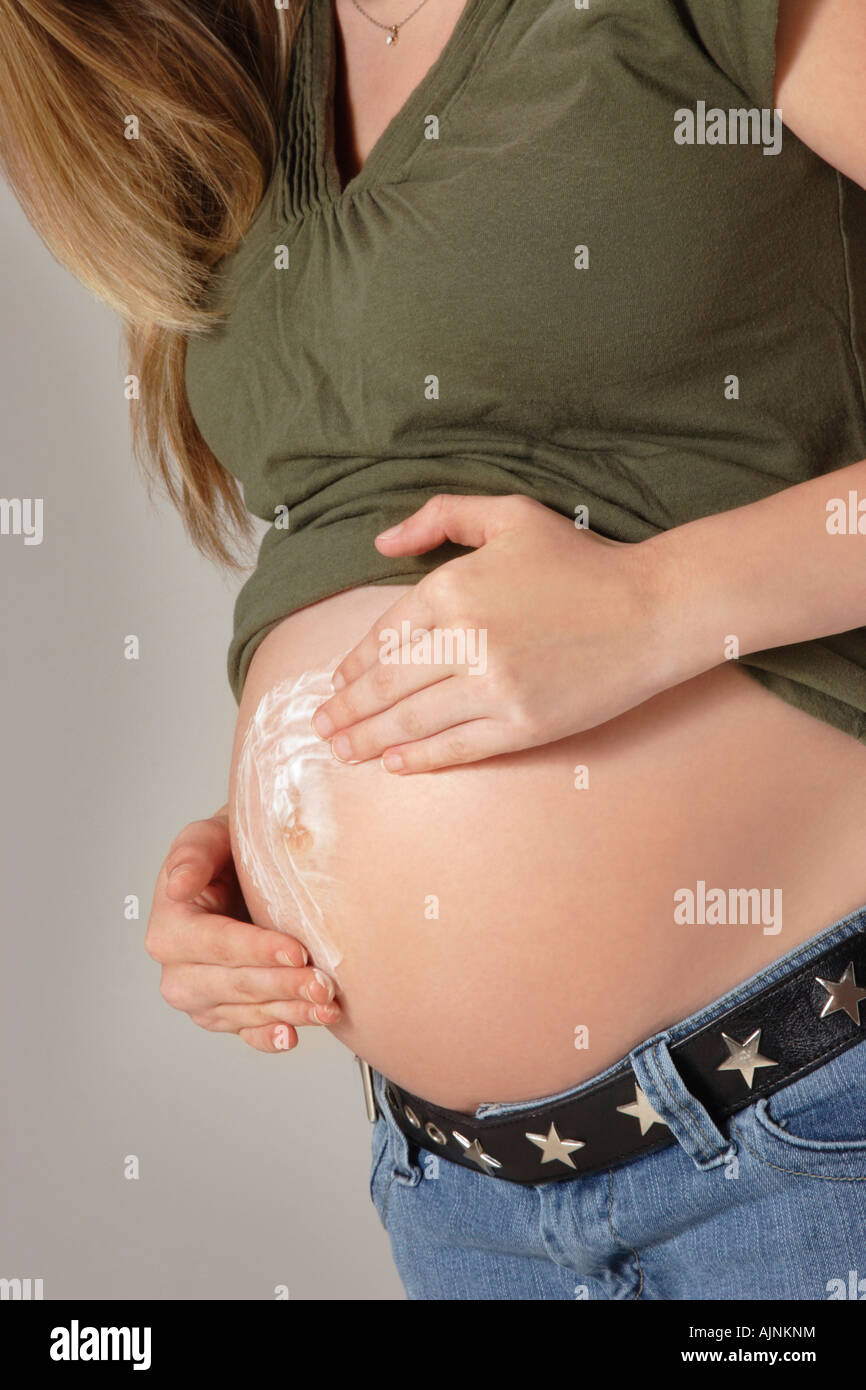 A pregnant woman applying cream on her belly Stock Photo