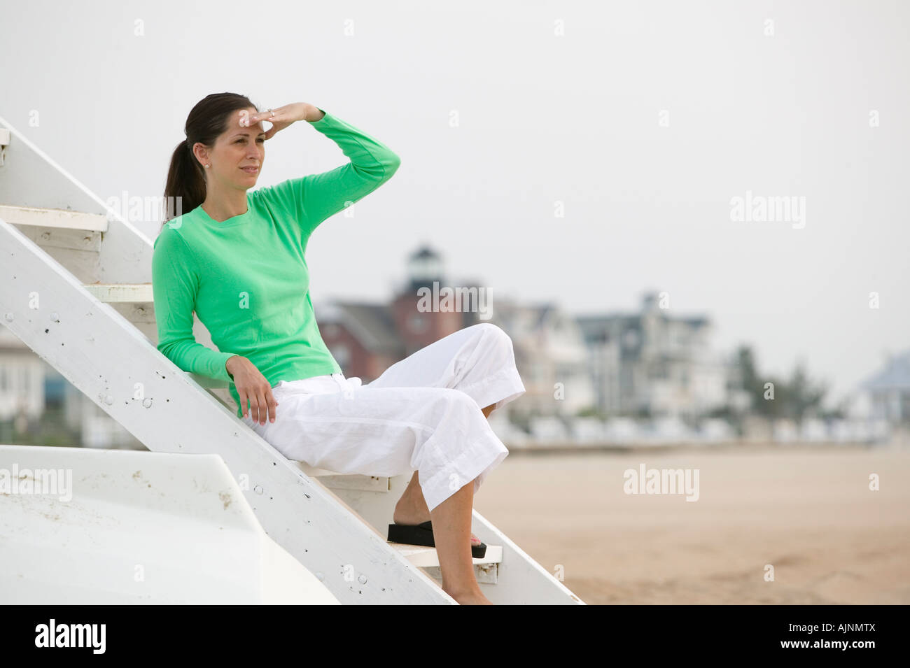 woman in mid 30s peers out to sea from a Lifeguard Chair in Sea Girt New Jersey Stock Photo