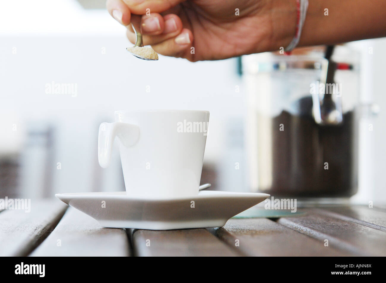 Woman putting sugar in a cup of coffee Stock Photo