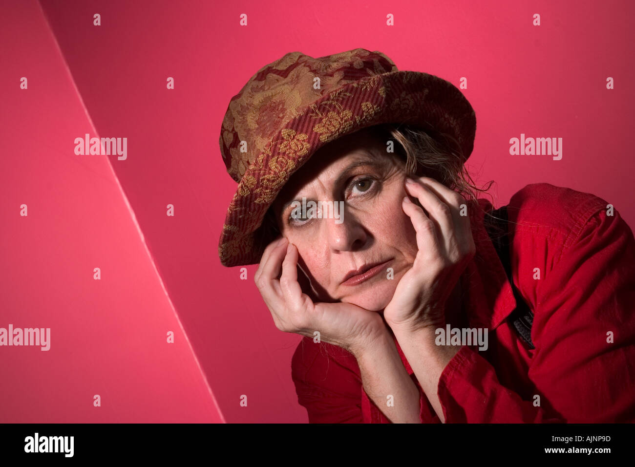 Middle age woman wearing a red dress and a hat sitting on a bed thinking Model Released  Stock Photo