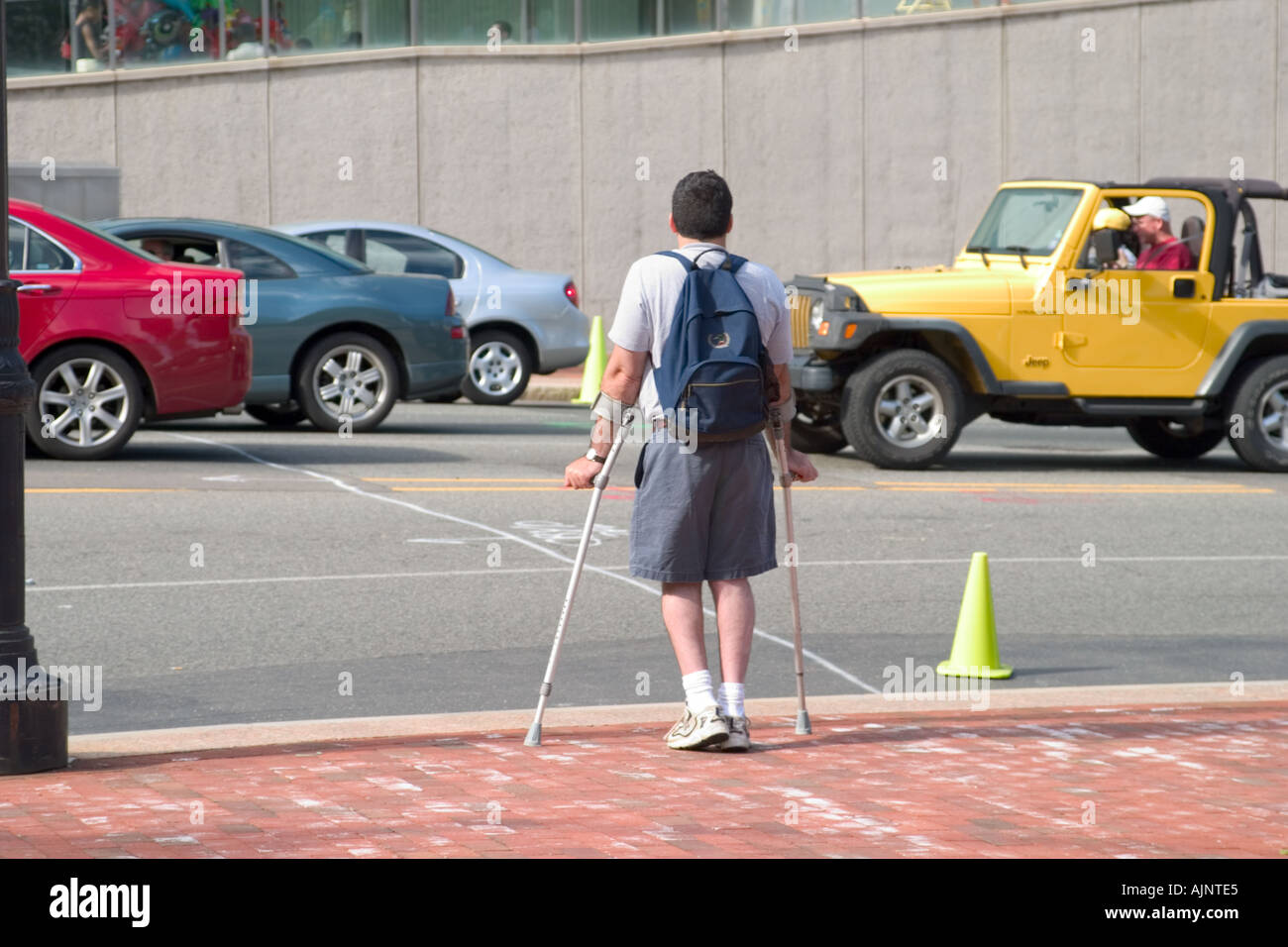 Man on crutches wearing a backpack waiting to cross a busy city street