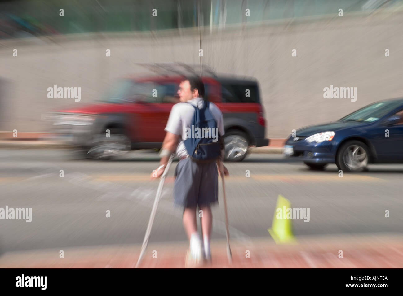 Man on crutches wearing a backpack waiting to cross a busy city street