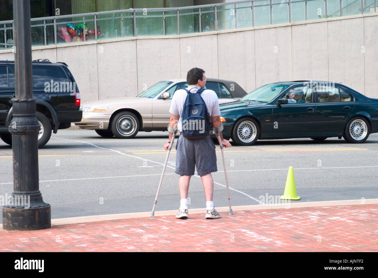 Man on crutches wearing a backpack waiting to cross a busy city street