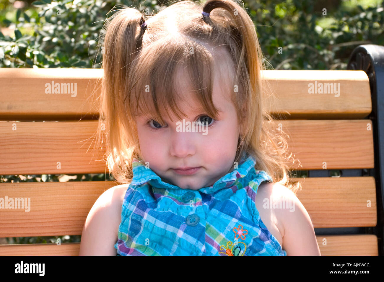 Young girl sitting on a wooden bench at a park Model Released Stock ...