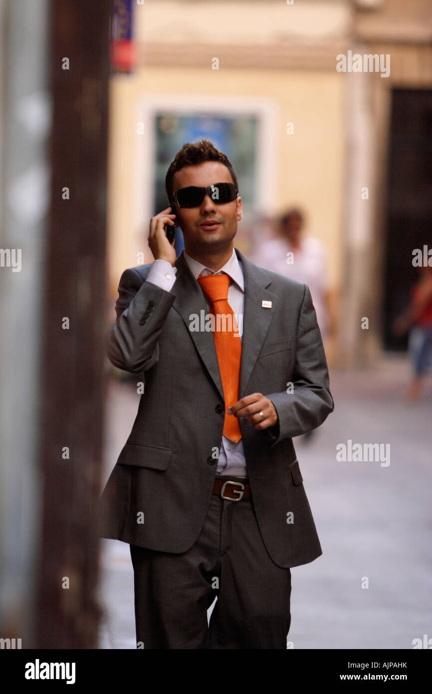 A smart young man in chic grey suit and dark sunglasses uses a mobile phone on the street in Palma de Mallorca, Spain. Stock Photo