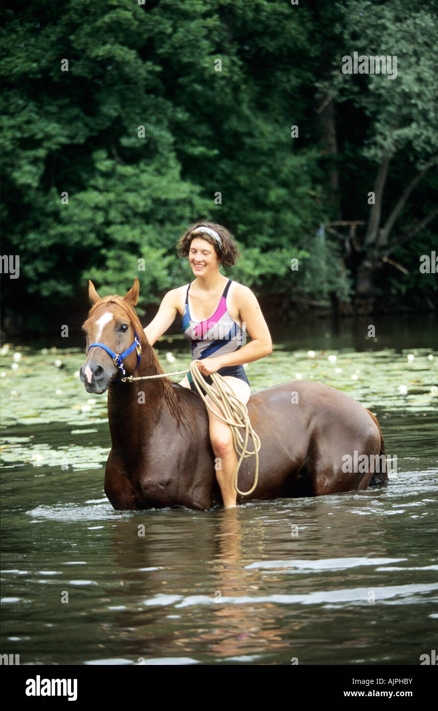 a girl is riding with a horse through a lake Stock Photo