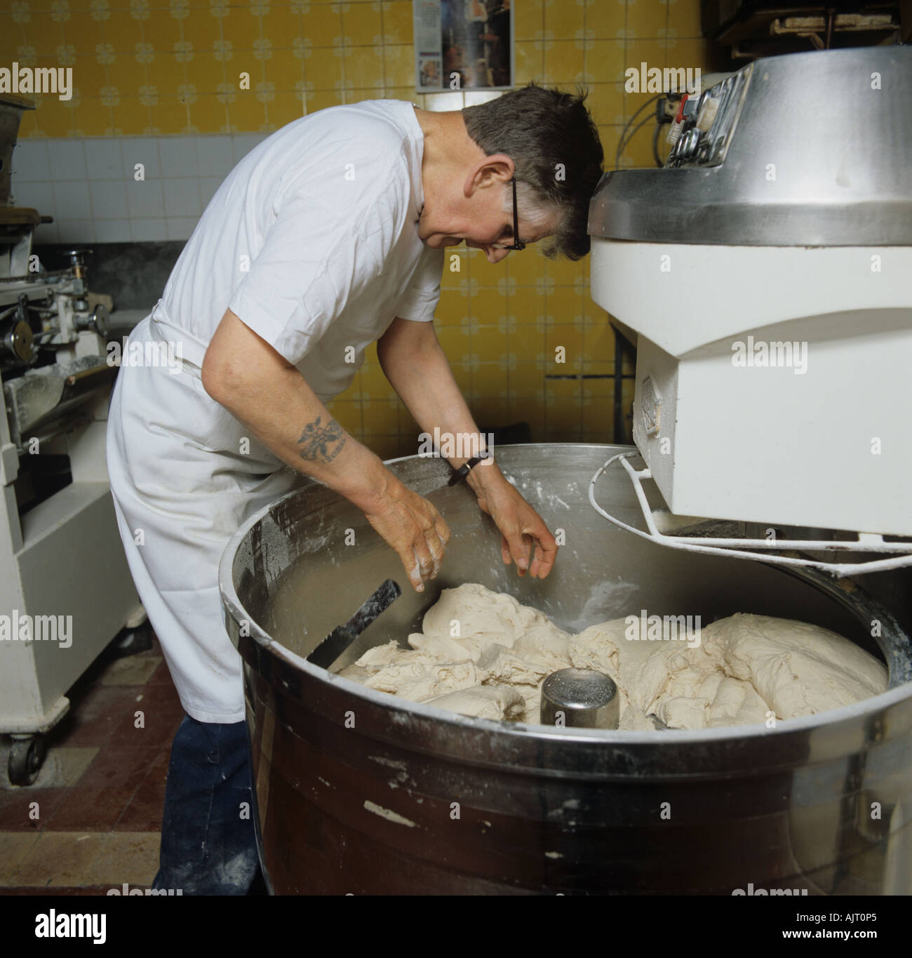 Baker removing dough from large machine for commercial bread making Stock Photo