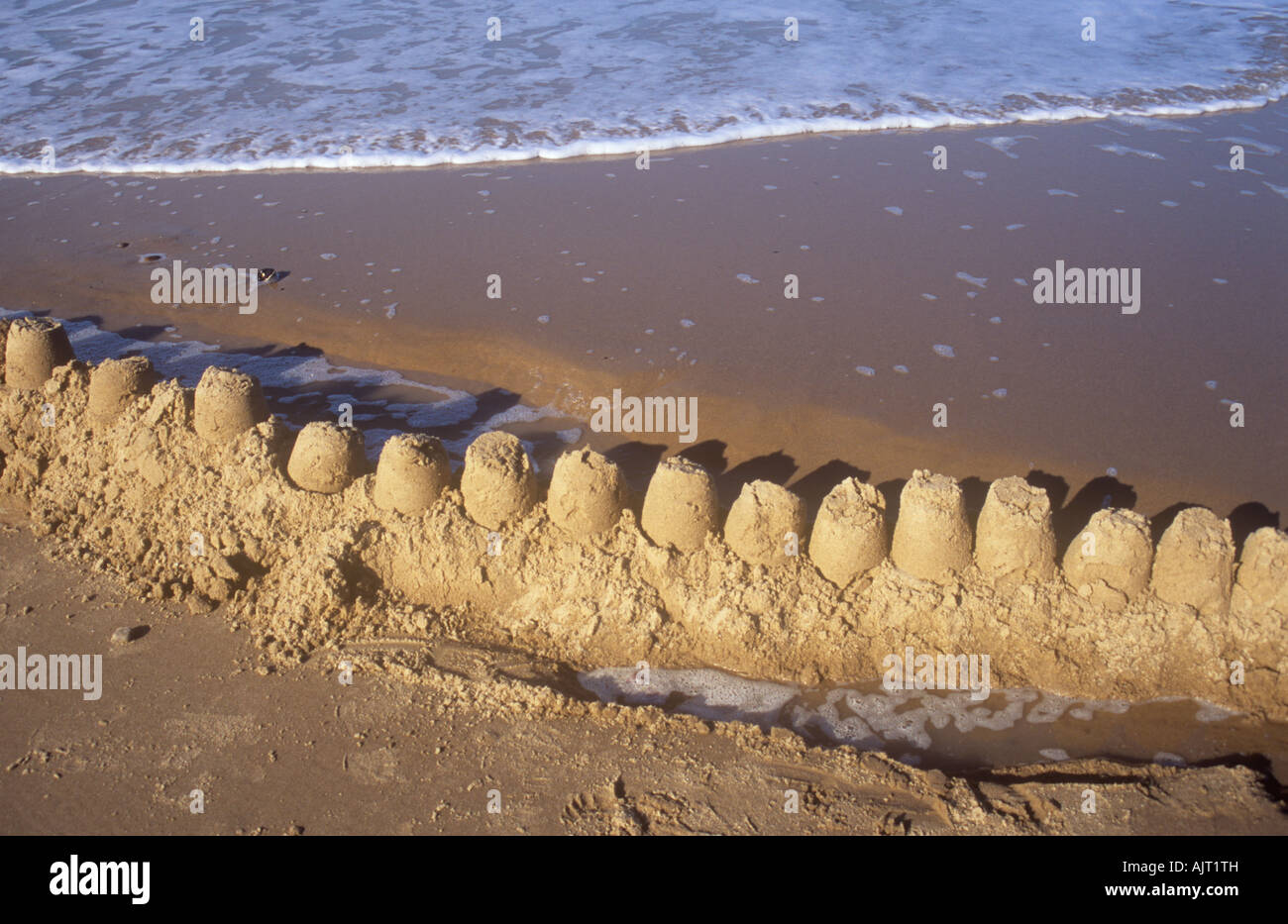 Row of fifteen sandcastles on sandy beach about to be inundated by incoming tide Stock Photo