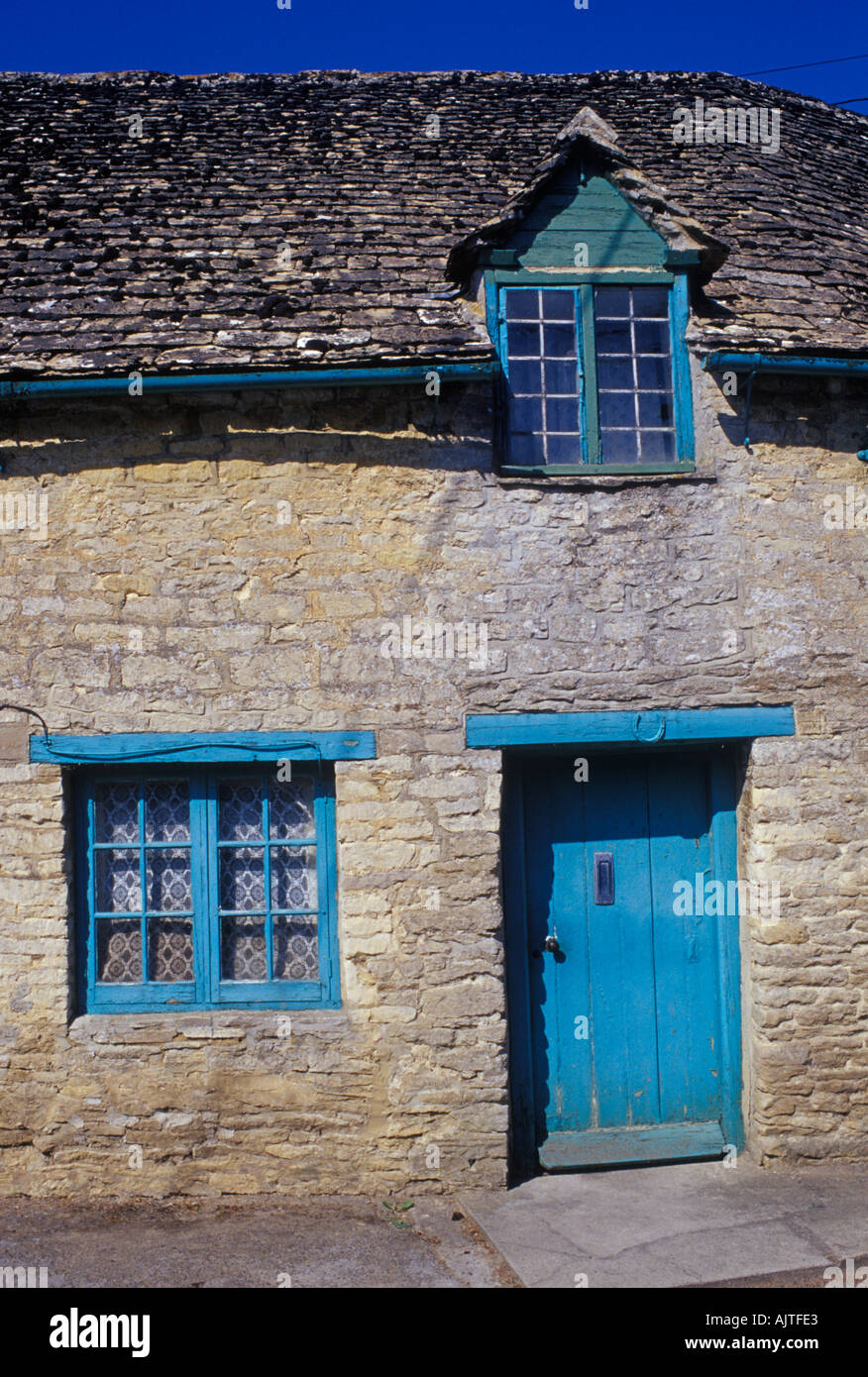 Asthall Oxfordshire Cotswold stone cottage in some disrepair lucky horseshoe over door bright turquoise paintwork Stock Photo