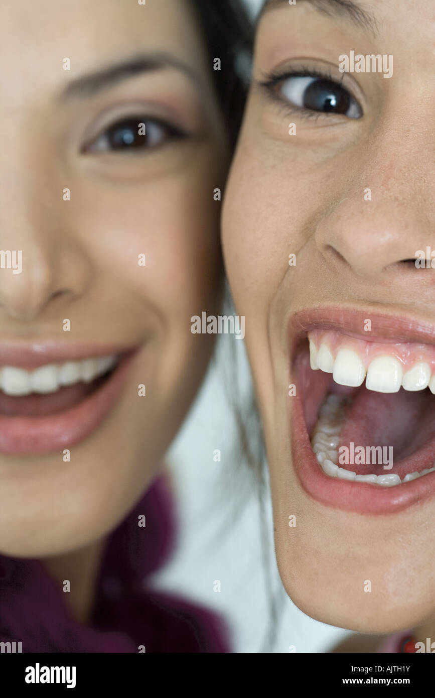 Two young female friends smiling with mouths wide open, looking at camera, extreme close-up of faces, cropped Stock Photo