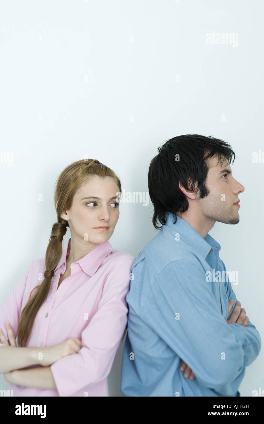 Young couple standing back to back with arms crossed, woman looking over shoulder, waist up, portrait Stock Photo