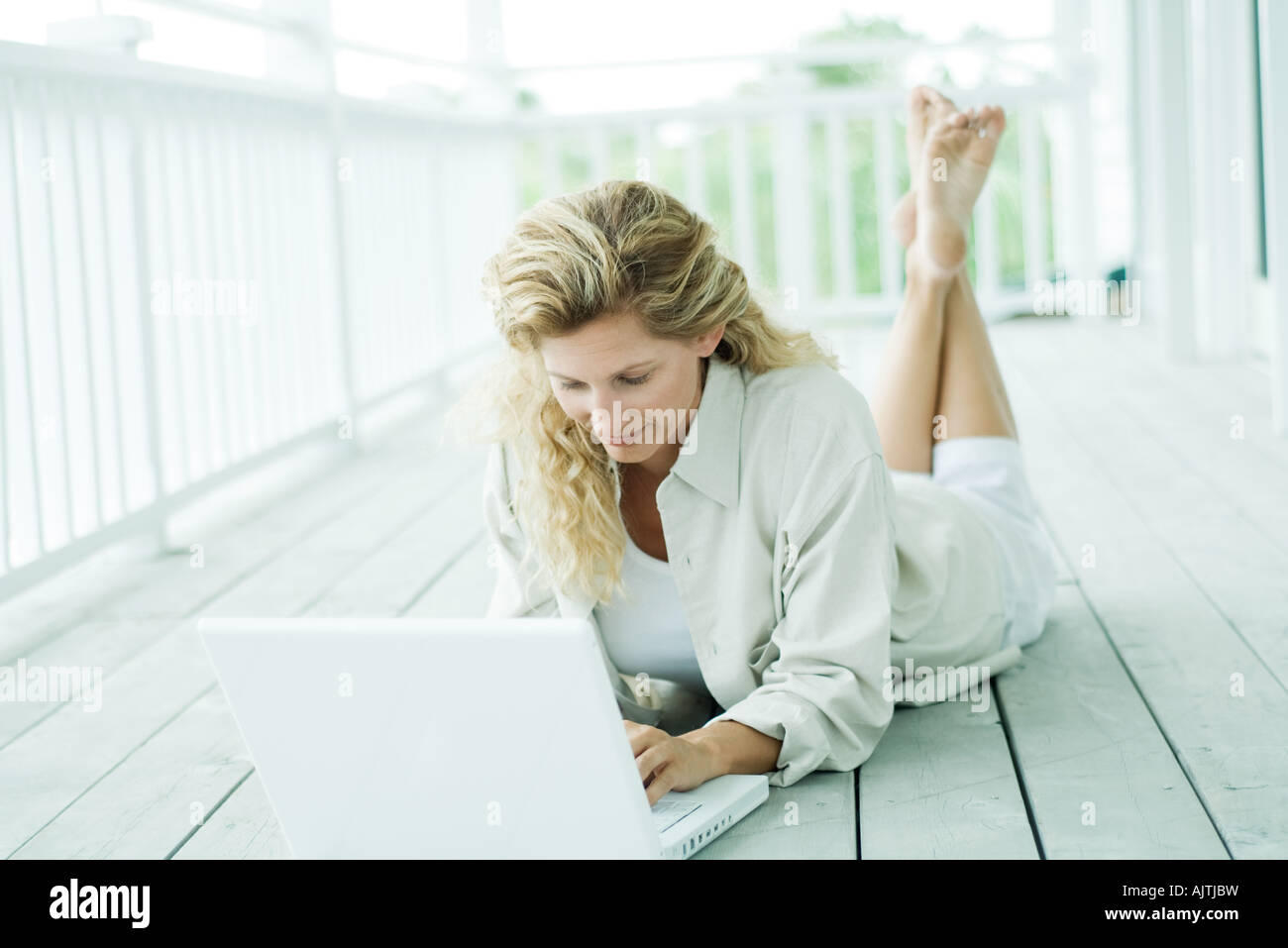 Woman lying on stomach on deck, using laptop, looking down Stock Photo