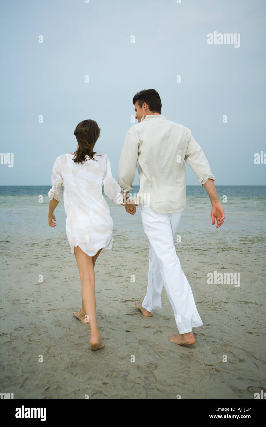 Father and daughter walking hand in hand on beach, rear view, full ...