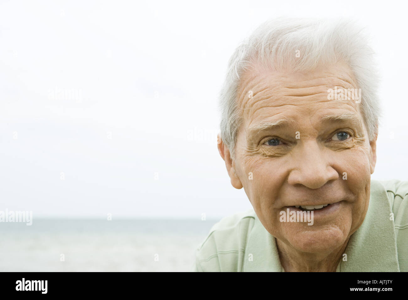 Senior man smiling, looking away, headshot, ocean in background Stock Photo