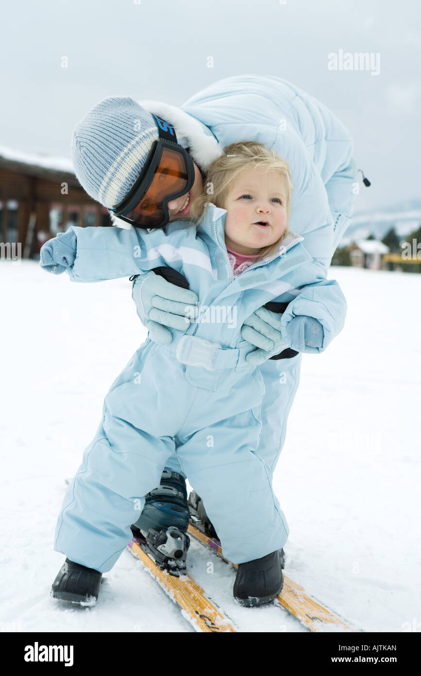 Teenage girl bending over, embracing toddler, both dressed in ski-suits Stock Photo