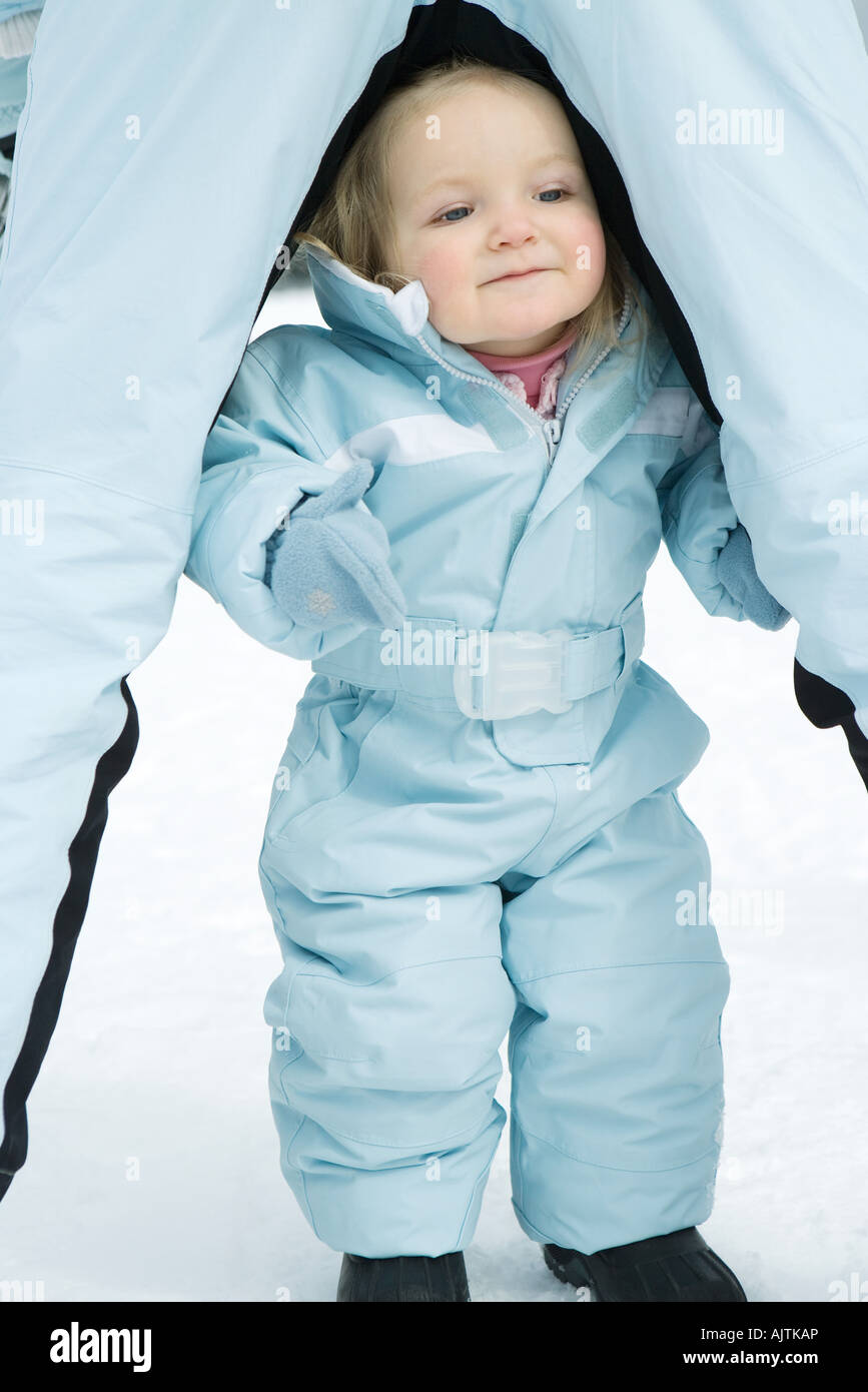 Toddler girl standing between sibling's legs, dressed in skisuit