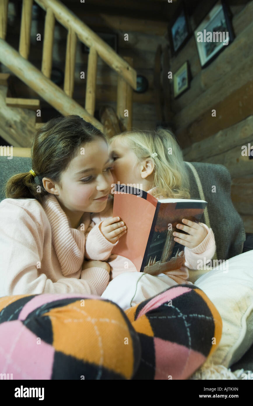 Preteen girl reading book with toddler, toddler whispering to her Stock Photo