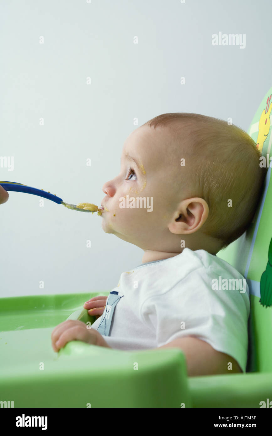 Baby sitting in high chair, being fed, looking up Stock Photo